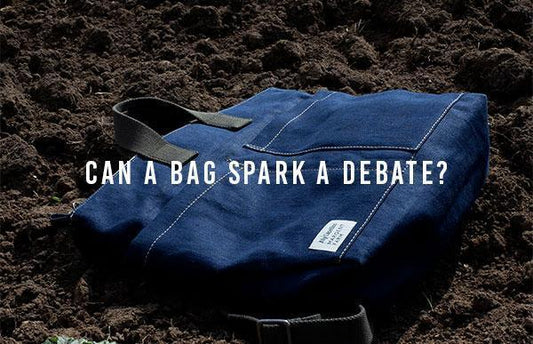A blue bag with white stitching and black stripes lies in some soil. Over the image is the text “CAN A BAG SPARK A DEBATE?”